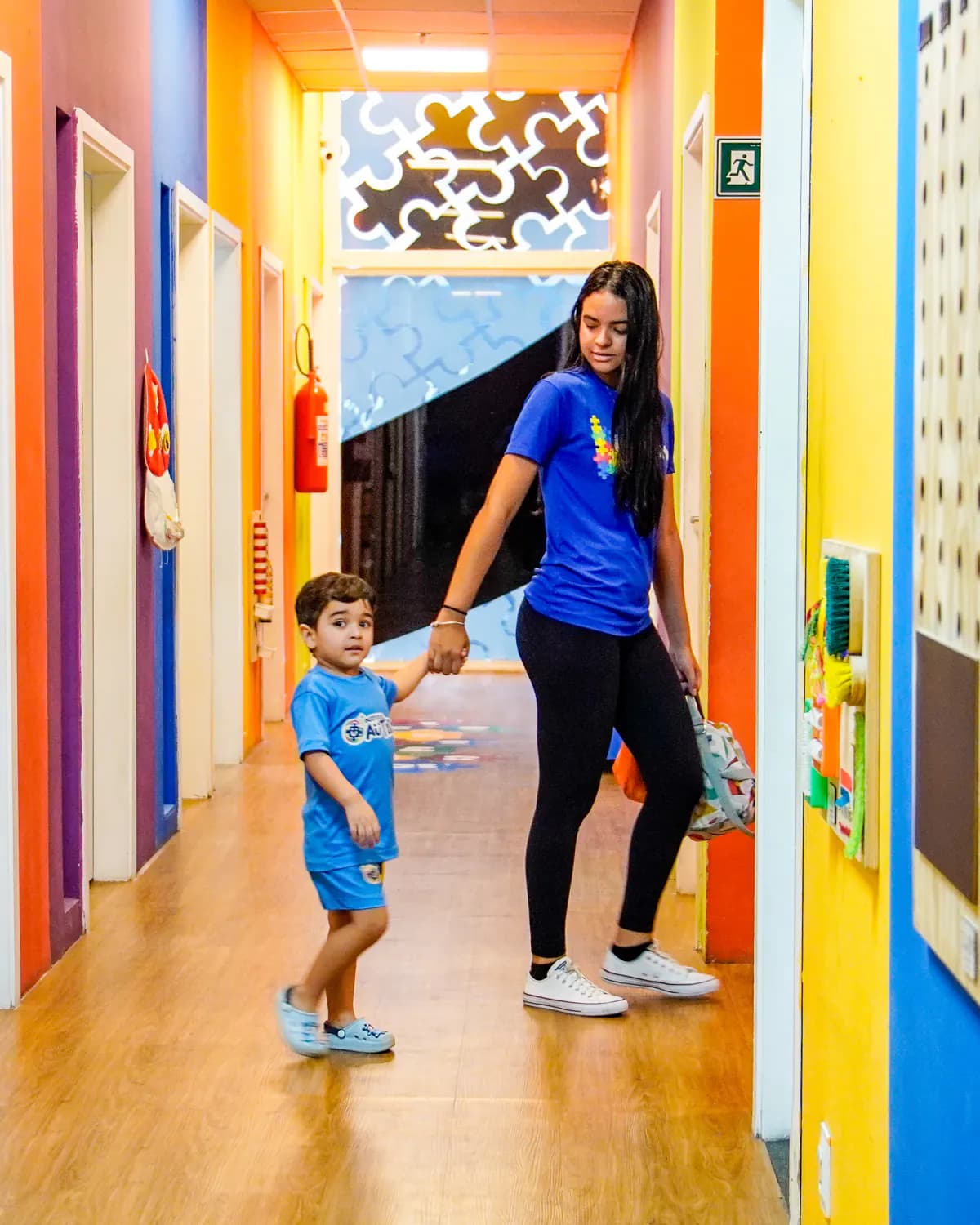 Terapeuta caminhando com criança por um corredor colorido do Instituto